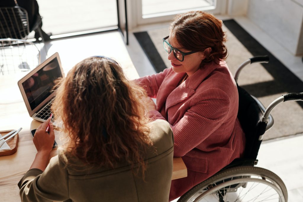 Imagen de dos mujeres utilizando un ordenador portátil. Una de ellas usa silla de ruedas.