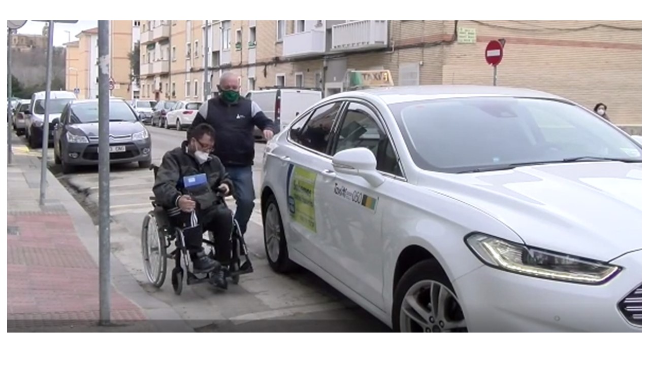Fotografía de un hombre usuario de silla de ruedas junto a un taxi de Pamplona. El conductor está yendo hacia el hombre para apoyarle en el traslado de la silla al taxi.