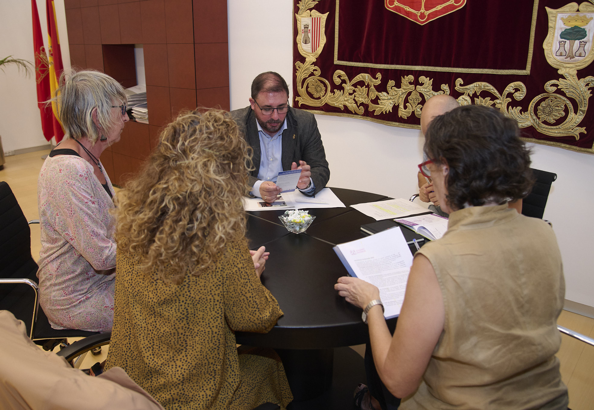 Foto de Unai Hualde, Victoria Erice, Idoia Lorea y Amelia Lecumberri sentados alrededor de una mesa, en un momento de su reunión. En la pared se ve el tapiz con el escudo de Navarra, y al fondo, las banderas de Navarra y de España.