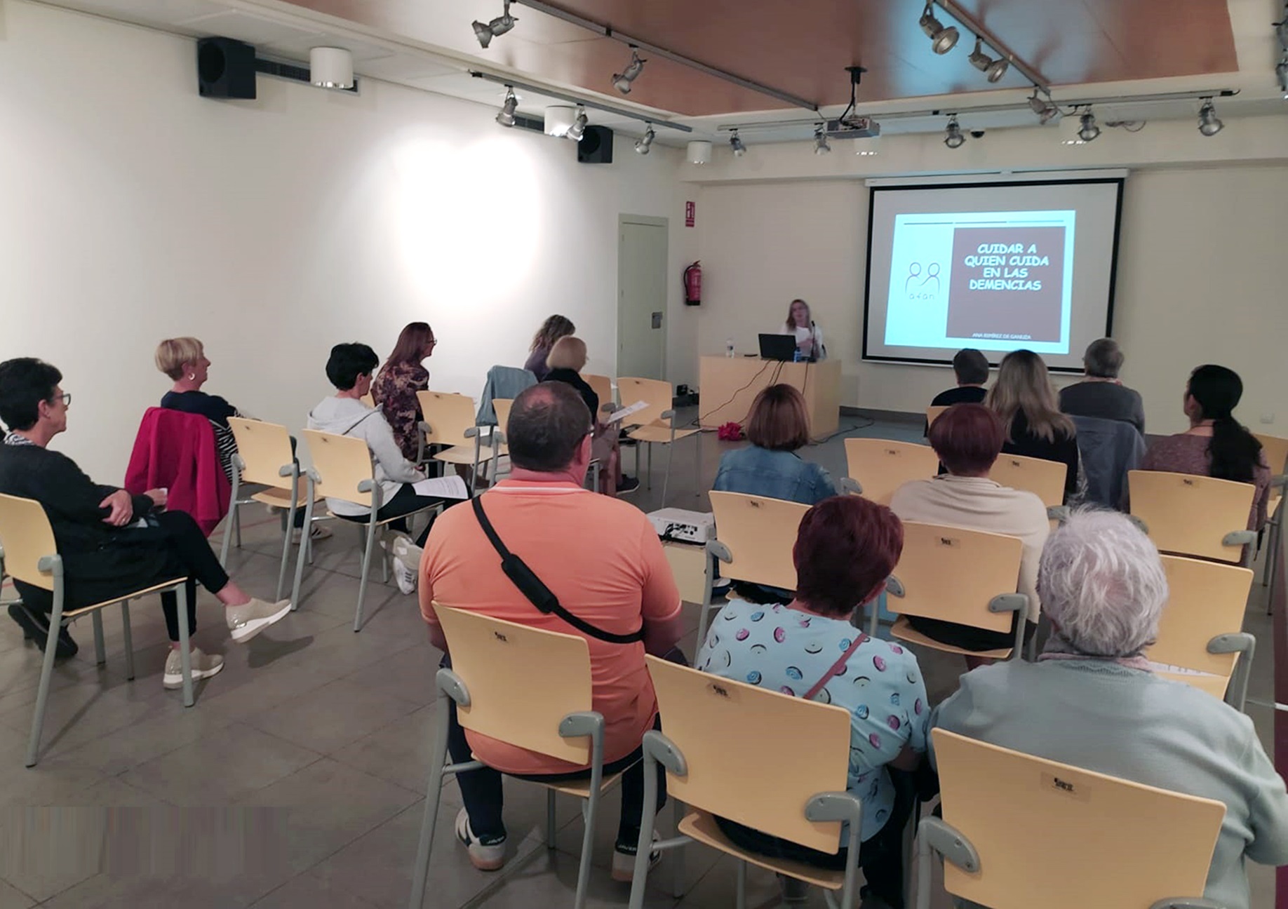 Fotografía del primer taller, en Castejón. Hay varias personas sentadas en un aula, mientras la instructora explica algo acompañándose de una diapositiva.
