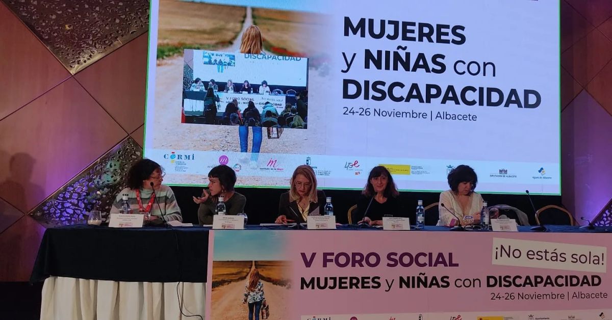 Momento del 'V Foro Social de Mujeres y Niñas con Discapacidad'. Hay cinco mujeres sentadas a una mesa, delante de una pantalla con el nombre del foro.