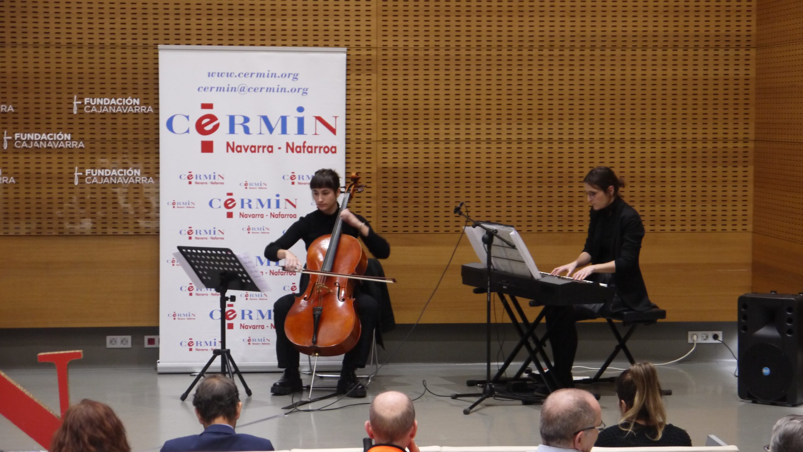 Dos mujeres tocando, respectivamente, un violoncello y un piano. Detrás de ellas está el logo de CERMIN.
