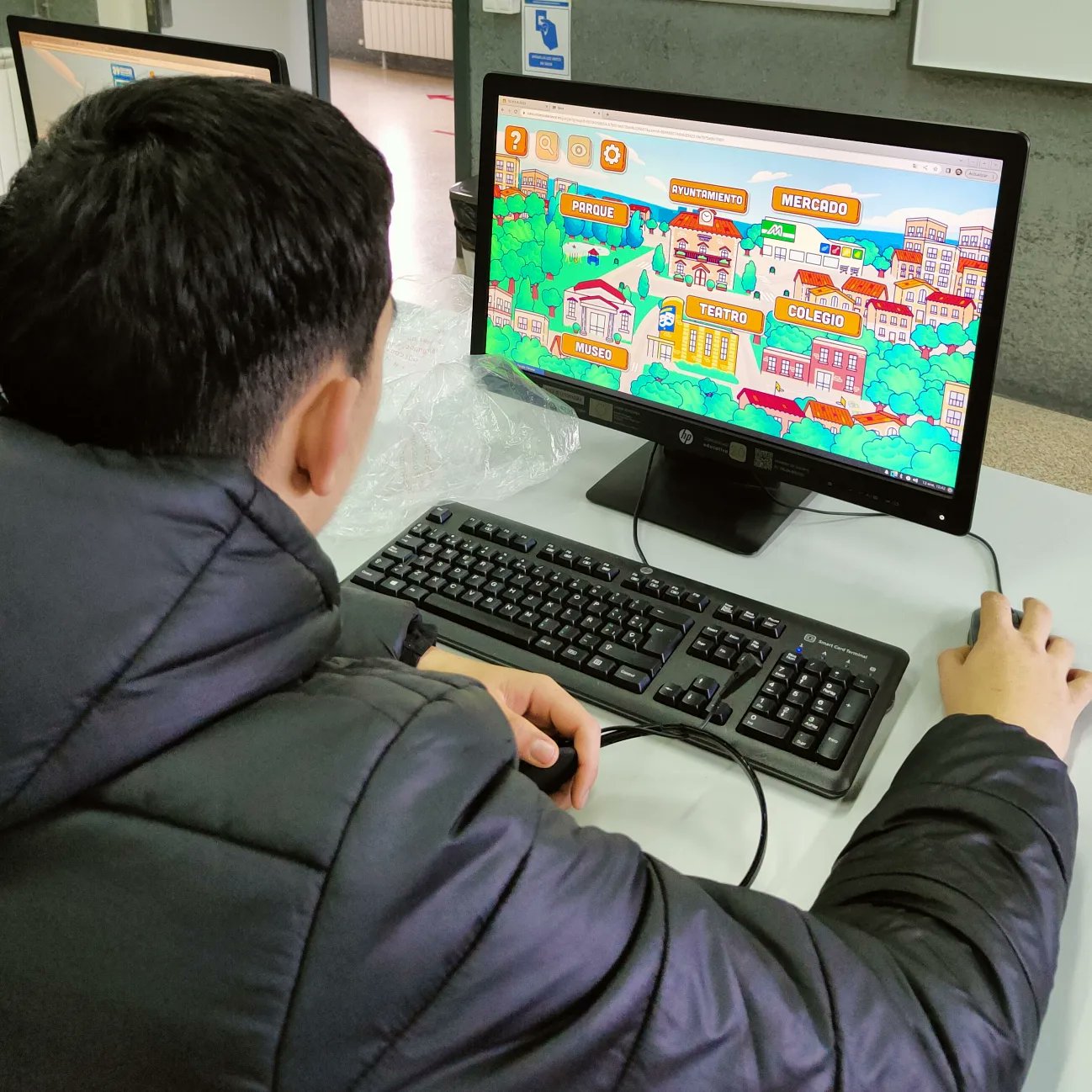 Escolar jugando a ONCITY en un ordenador. En el videojuego aparece una localidad y hay destacados varios sitios que se pueden visitar: parque, museo, teatro, colegio, mercado y ayuntamiento.