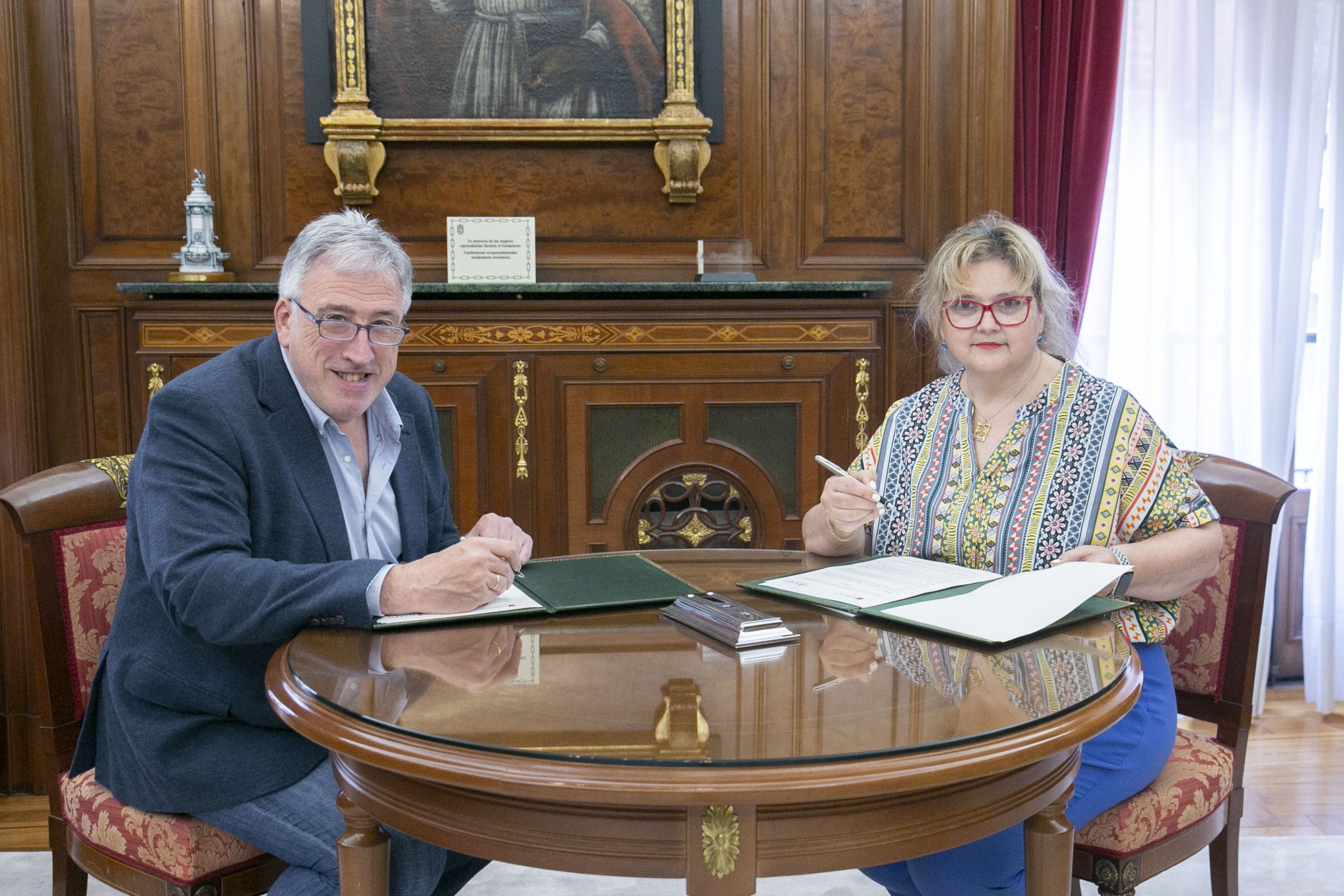 Momento de la firma del convenio en el que se encuentran sentados con los documentos del Convenio: el alcalde, Joseba Asiron y la vicepresidenta del CERMIN, Cristina Mondragón.