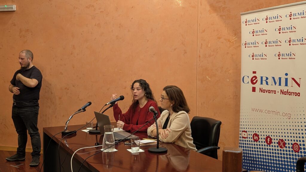 LAS PONENTES SENTADAS HABLANDO EN LA SESIÓN. DETRÁS ROLL UP DE CERMIN Y A LA IZQUIERADA ILSE