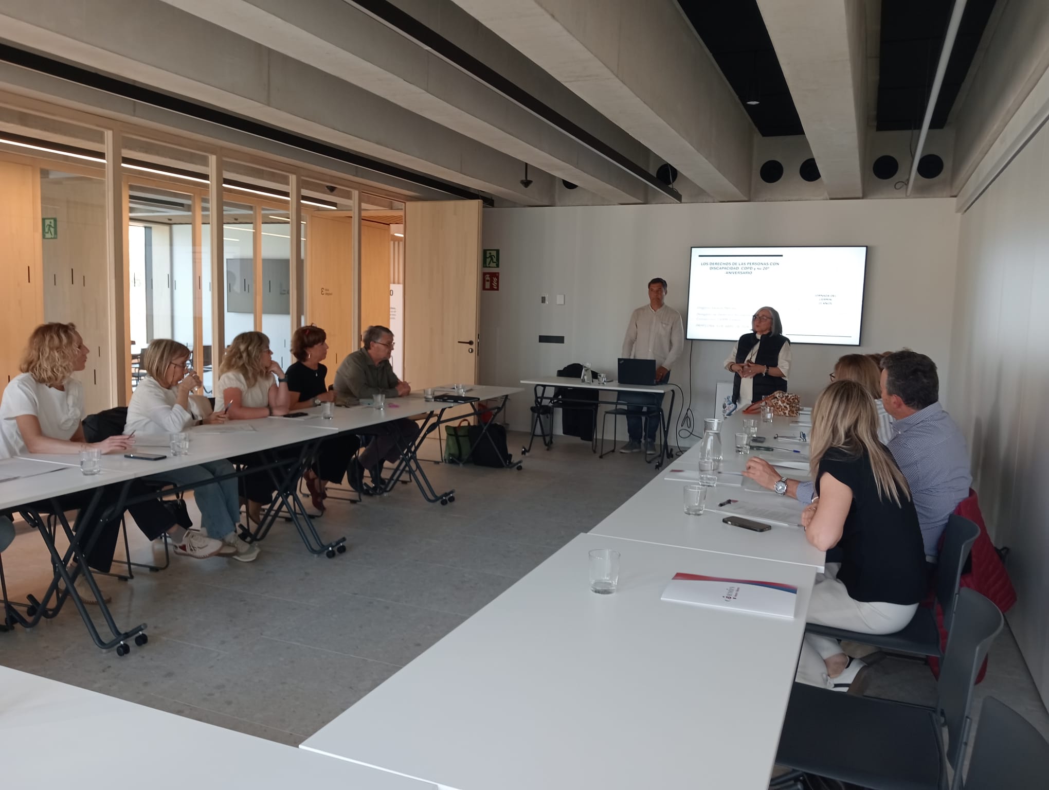 PERSONAS EN LA FORMACION ALREDEDOR DE UNA MESA EN FORMA DE U. DELANTE EL PONENTE Y LA PANTALLA