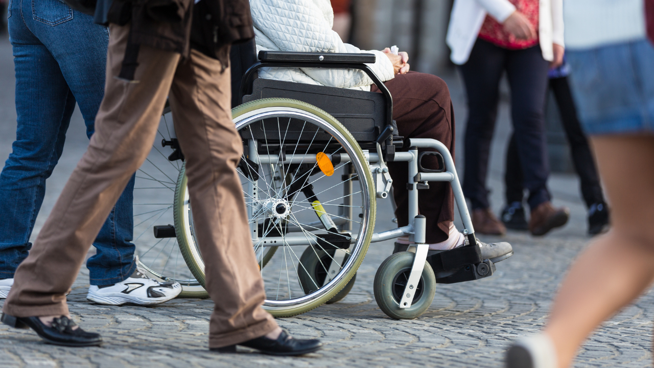 personas andando en la calle y entre ellas una persona en silla de ruedas