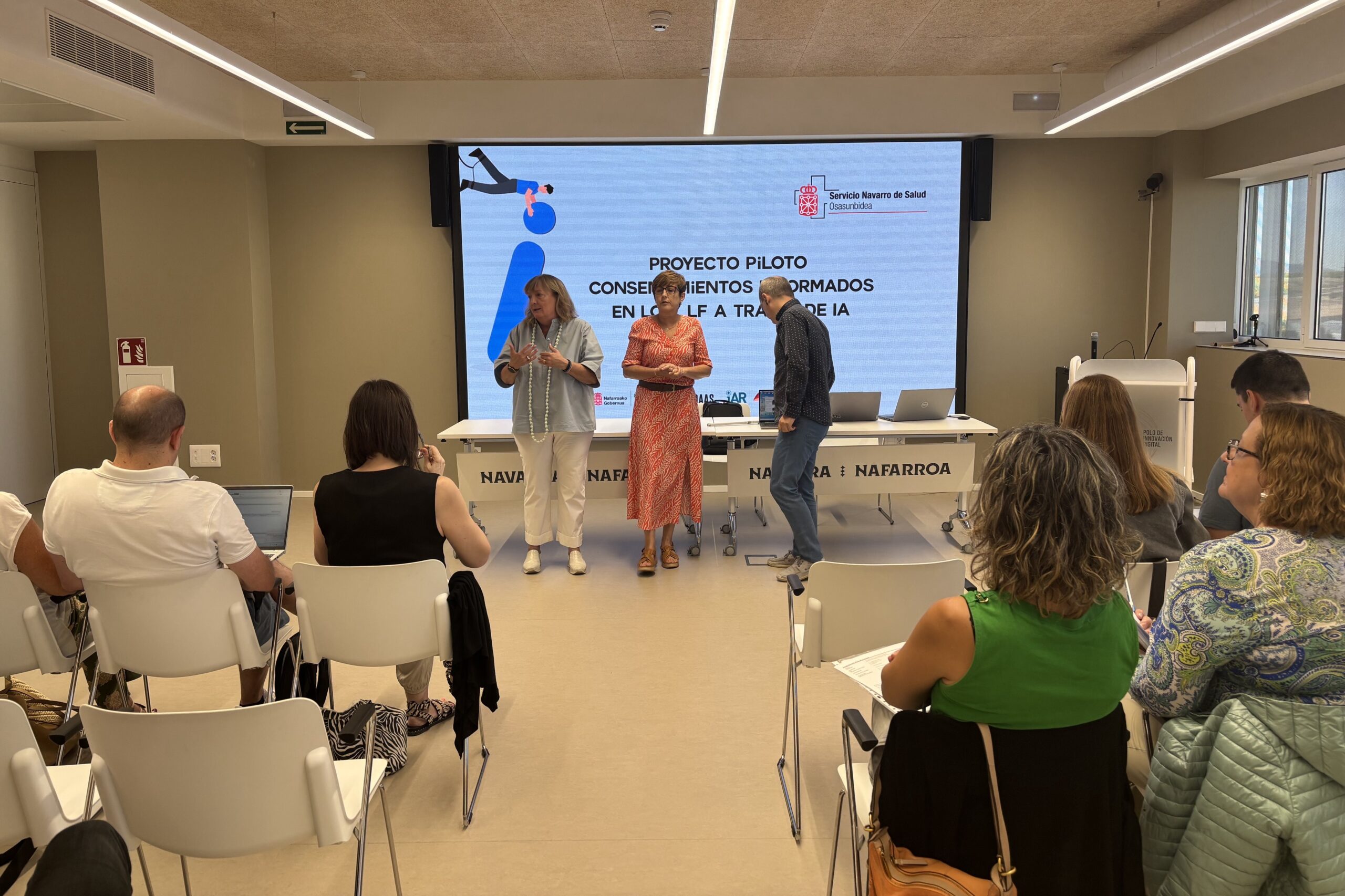 TRES PERSONAS PRESENTANDO DELANTE DE UNA PANTALLA DONDE SE PROYECTA EL MENSAJE